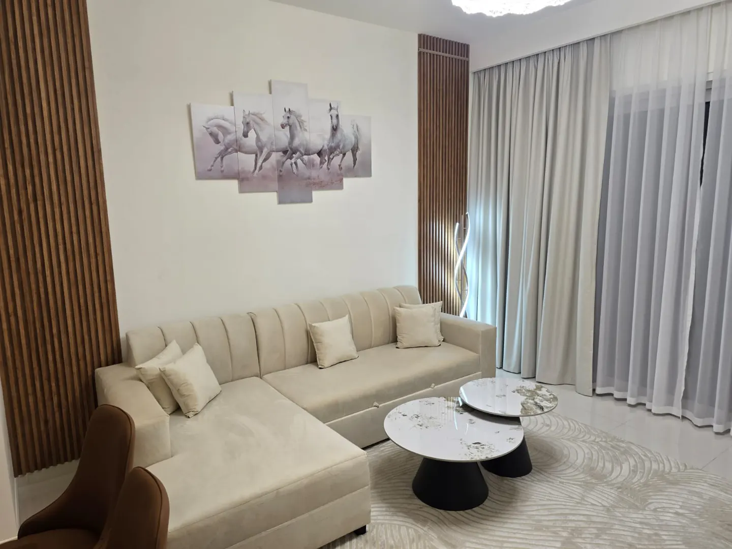 Living room with a beige sectional sofa, two round tables, and a horse painting on the wall.