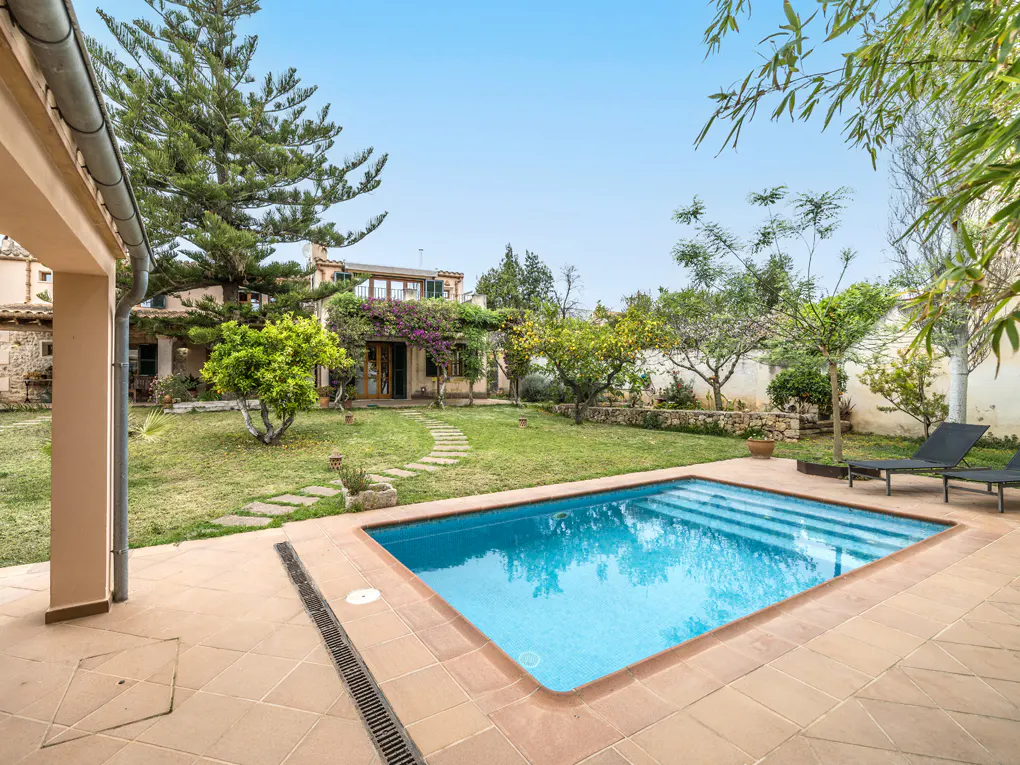 Backyard view of a house with a blue swimming pool, green grass, trees, and a stone path.