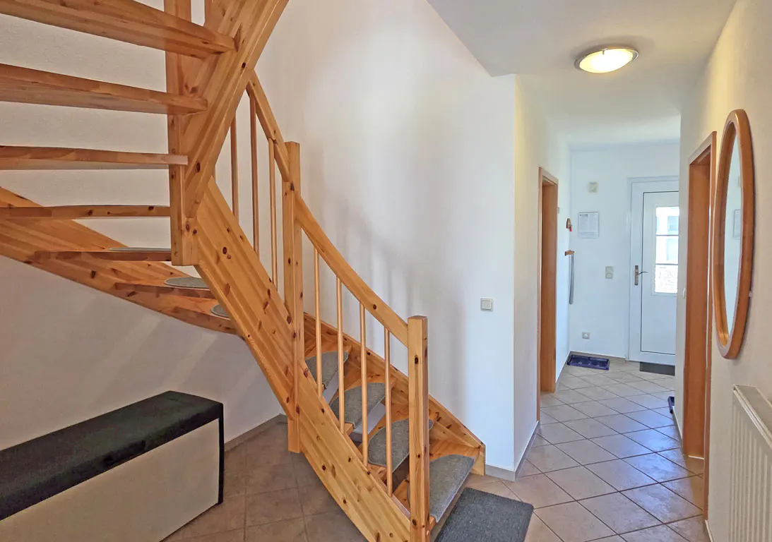 Interior view of a home featuring a wooden staircase with gray treads, a hallway with tile flooring, and a white front door.