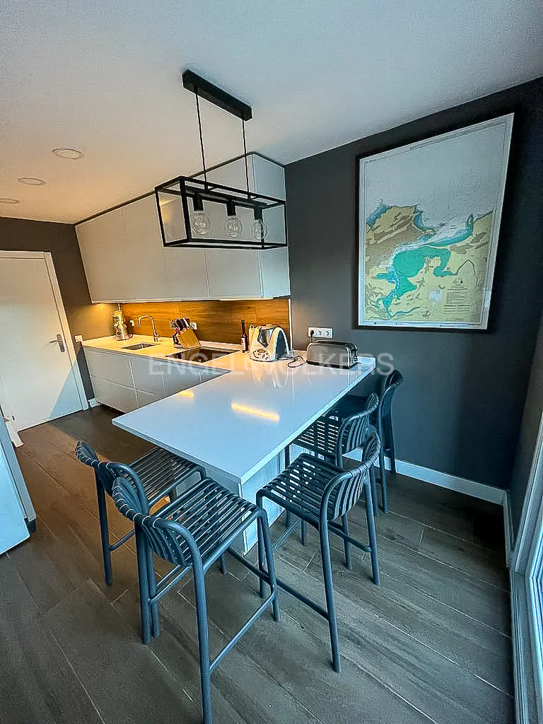 A modern kitchen with a white island, gray stools, and a black rectangular light fixture. A map hangs on the gray wall.
