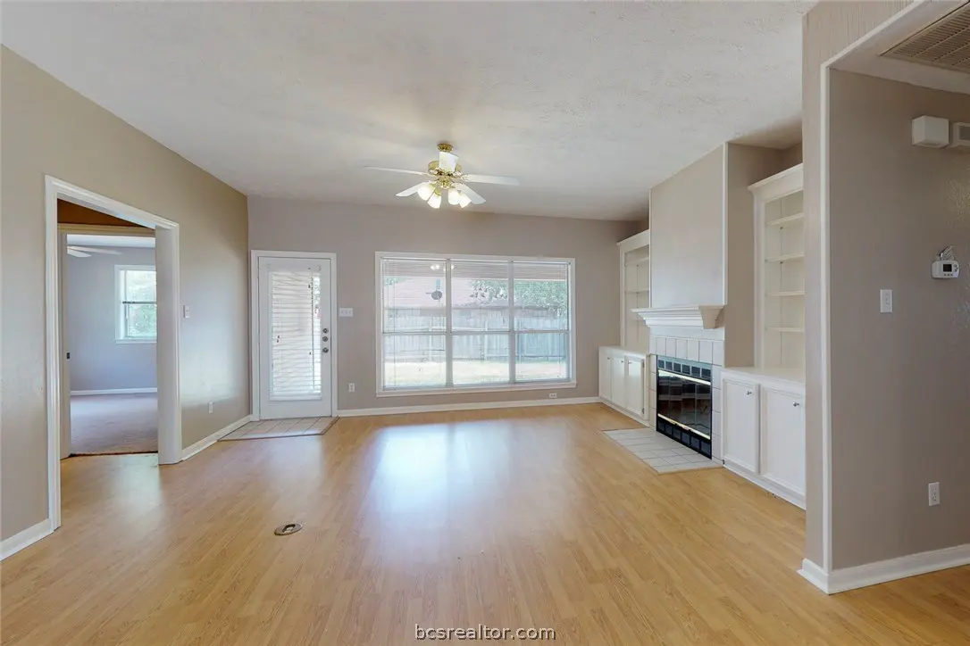 A living room with wood floors, a fireplace, built-in shelves, and a ceiling fan.
