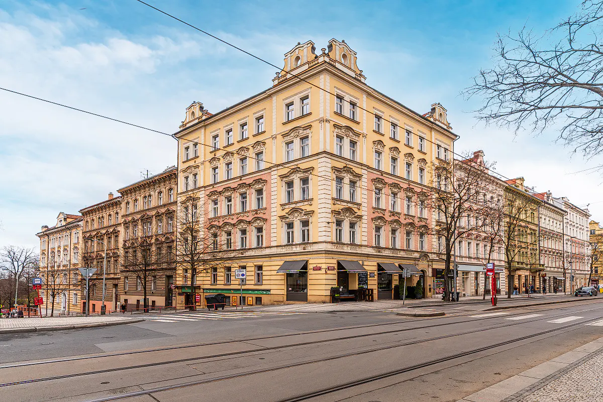 Street view of a yellow and pink corner building with a black awning in Prague, Czech Republic.