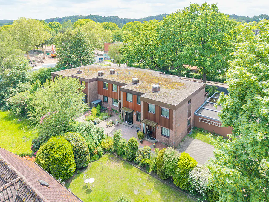 Aerial view of a row of brown brick townhouses with green lawns and trees. Construction site visible in the background.