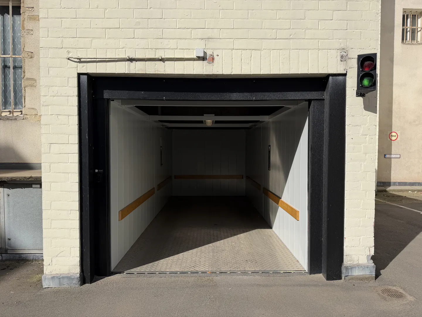 Open car elevator with black frame and white interior. A traffic light with a green light is on the right.