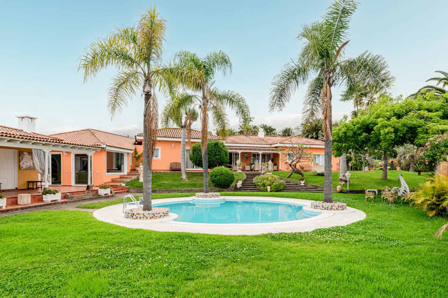 Exterior view of an orange house with a red tile roof, a round pool, and palm trees.
