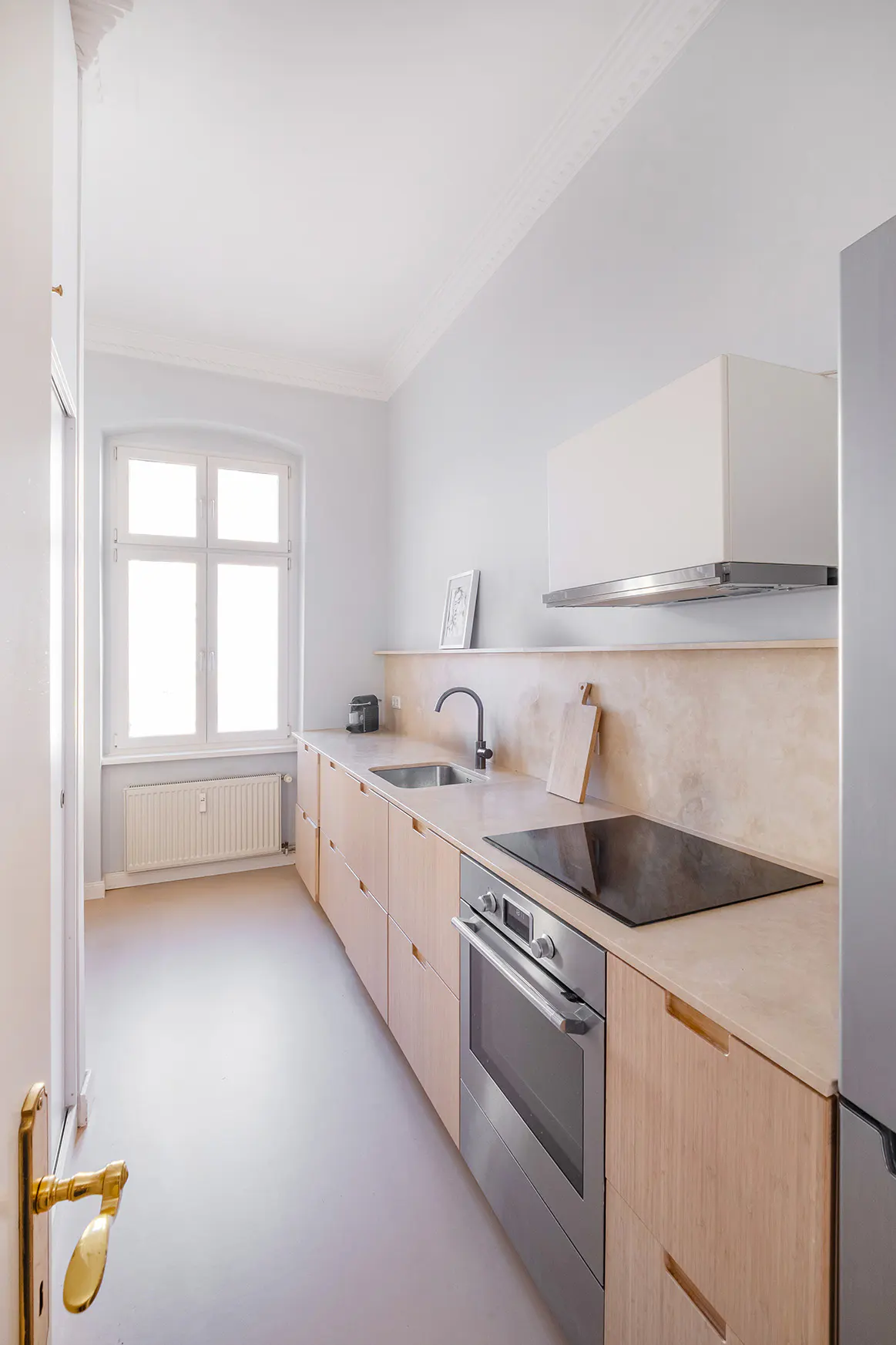 Bright kitchen with light wood cabinets, stainless steel oven and black cooktop. A window provides natural light.