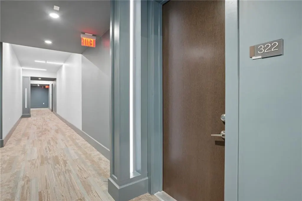 Hallway view with wood-look flooring, gray walls, and a brown door labeled "322". An exit sign is visible down the hall.