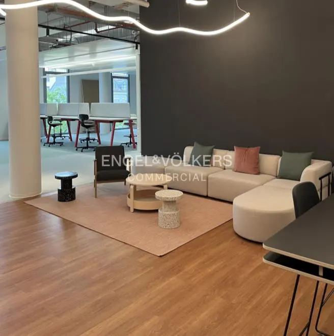 Office space with a beige sectional sofa, a dark gray accent wall, and a light wood floor.