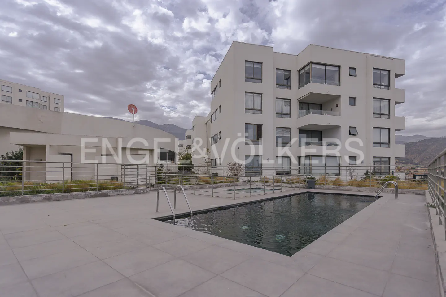 Rooftop pool with metal ladder in front of a modern white apartment building on a cloudy day.
