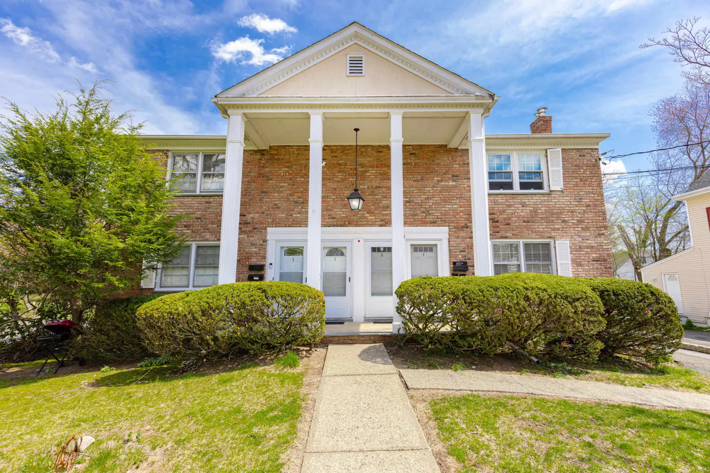 Two-story brick apartment building with white columns and doors under a blue sky.
