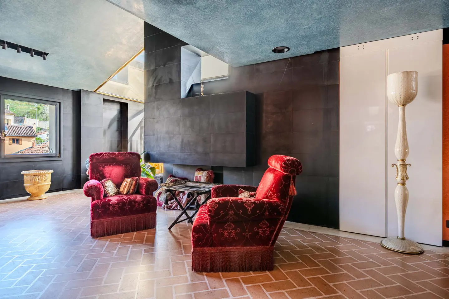 A living room with red velvet chairs, a black wall, and a herringbone brick floor.