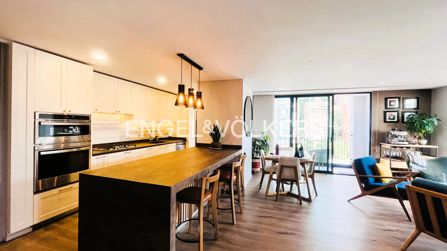 Modern open-plan kitchen with a dark island, white cabinets, and dining area leading to a balcony with city views.
