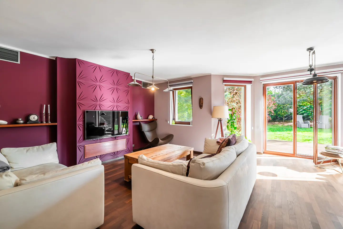 Bright living room with white sofas, wood floors, and a burgundy accent wall with a TV. Sliding glass doors lead to a green backyard.