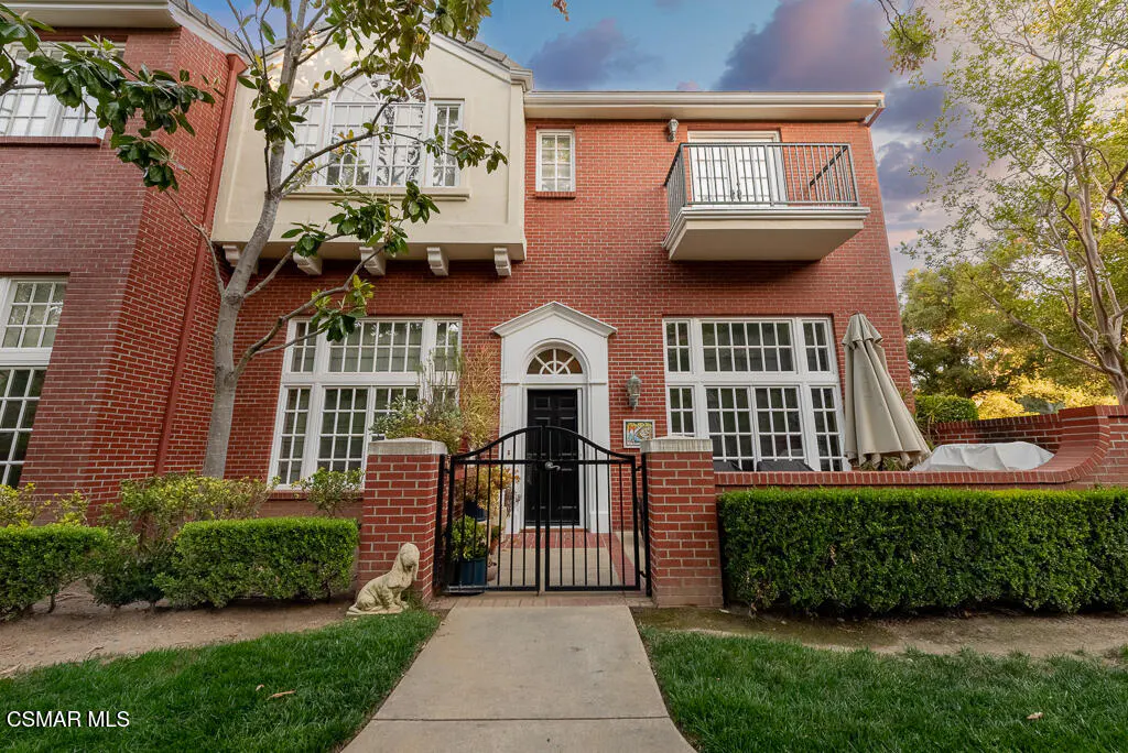 A three-story red brick house with a black gate, green lawn, and manicured hedges.