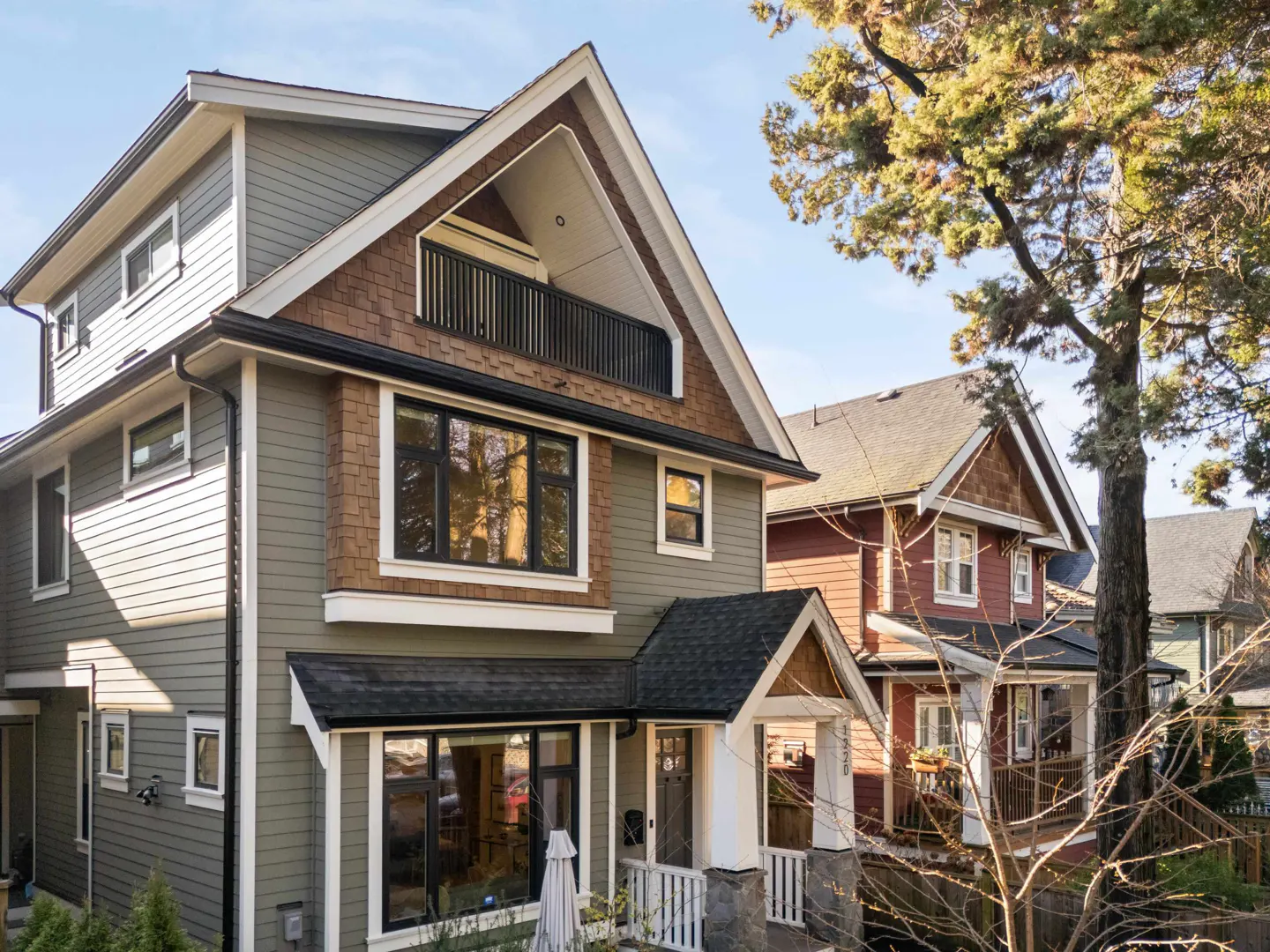 Exterior of a two-story house with olive green siding, brown shingles, black trim, and a small balcony.