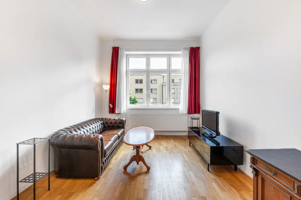 Living room with a brown leather sofa, oval wooden coffee table, black TV stand, and red curtains over a large window.