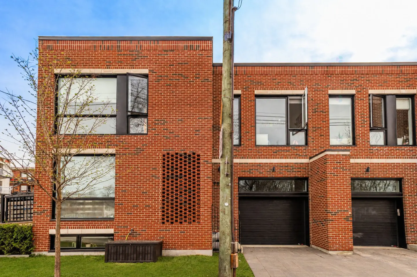 Modern red brick townhouses with black garage doors and window frames under a blue sky.