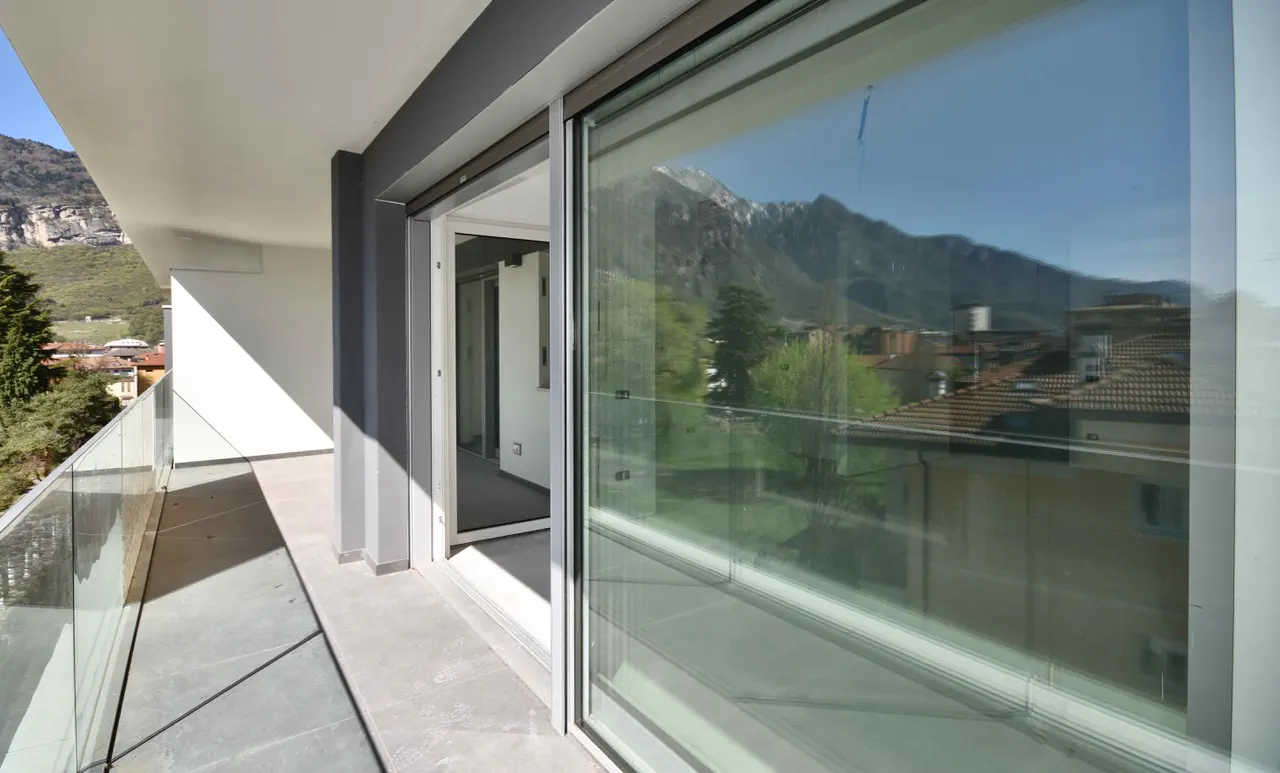 Balcony view with sliding glass doors open to a room. Mountains and buildings are reflected in the glass.