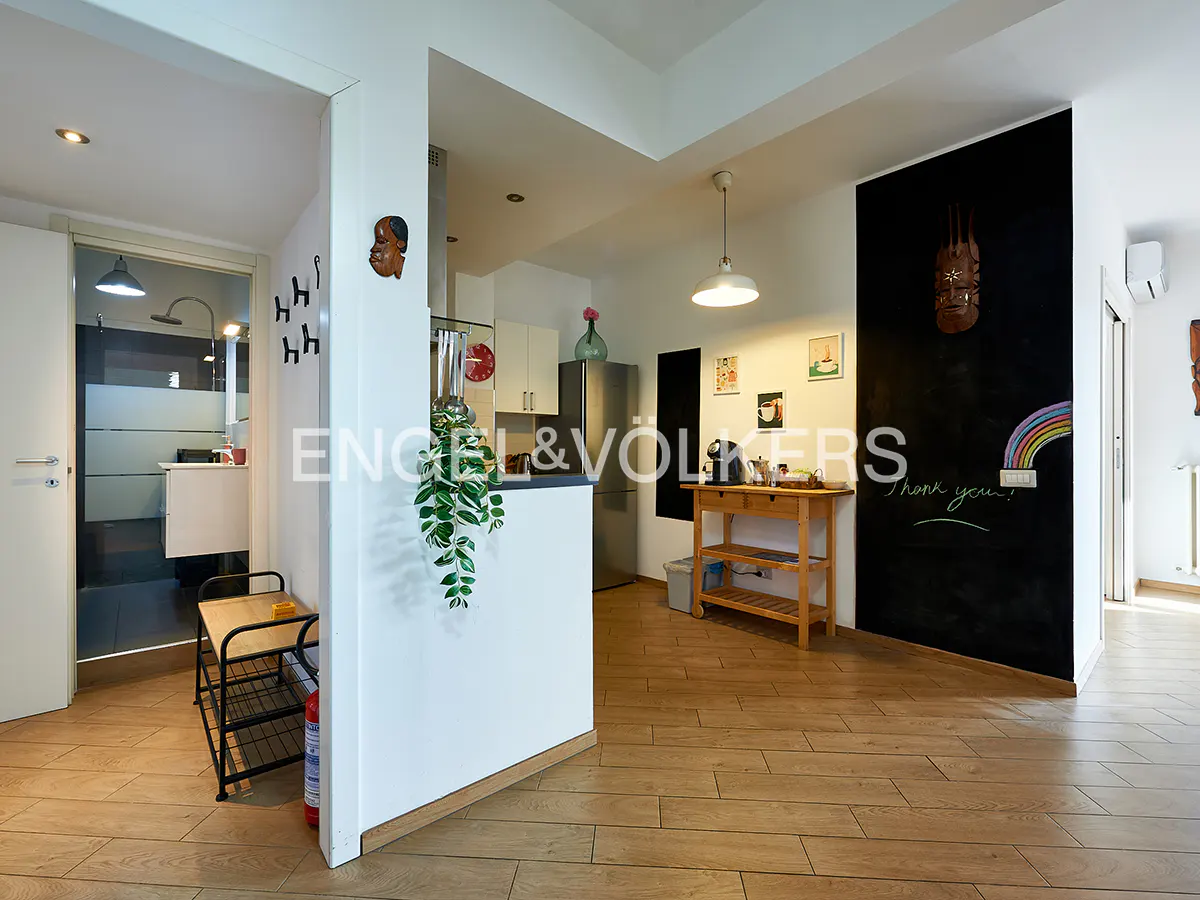 Open-concept apartment with wood floors, white walls, and a black chalkboard wall with a rainbow drawing. A small kitchen is visible in the background.