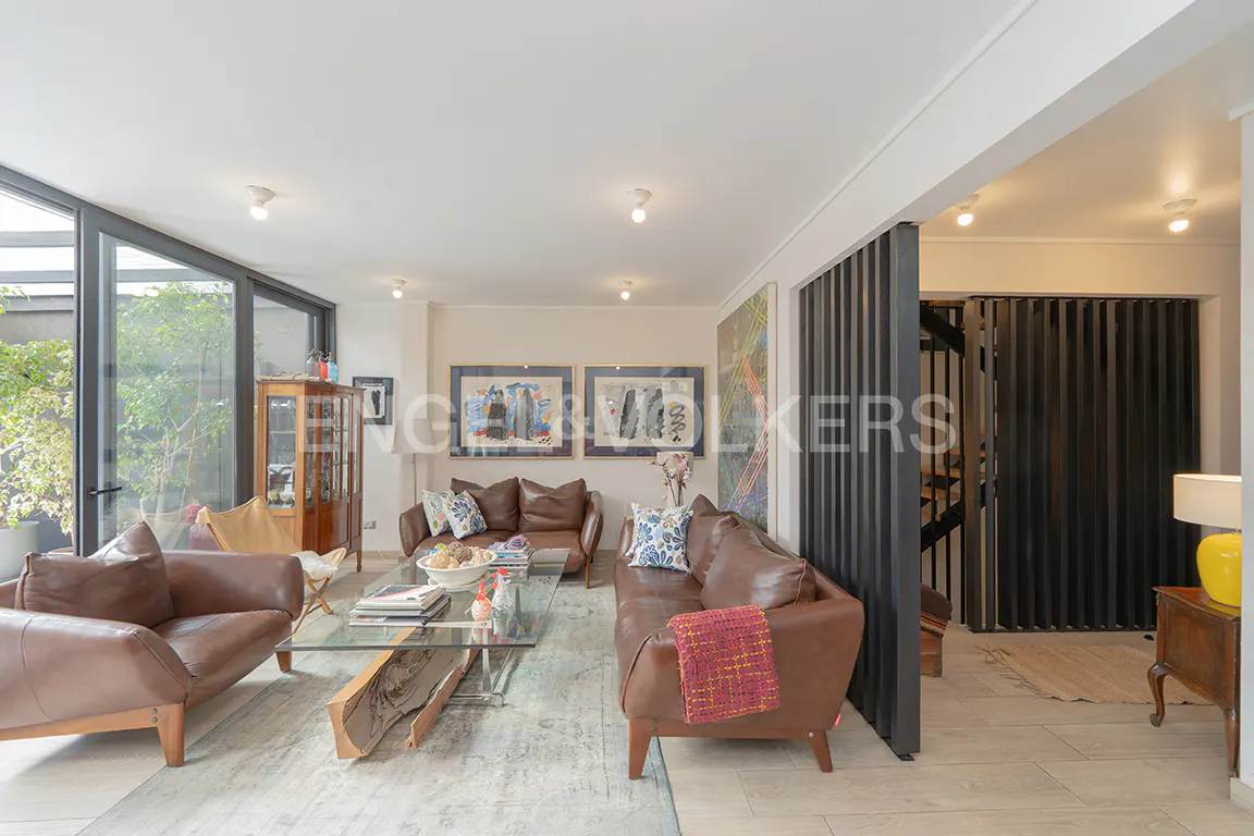 Bright living room with brown leather sofas, glass coffee table, and art. Black slatted wall and large windows add modern touches.