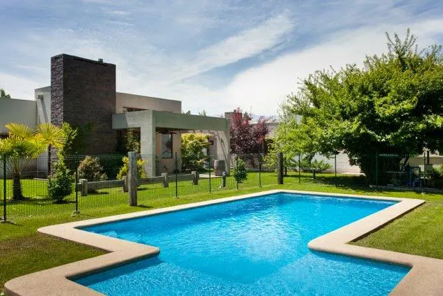 A modern house with a blue swimming pool in the backyard, surrounded by green grass and trees.
