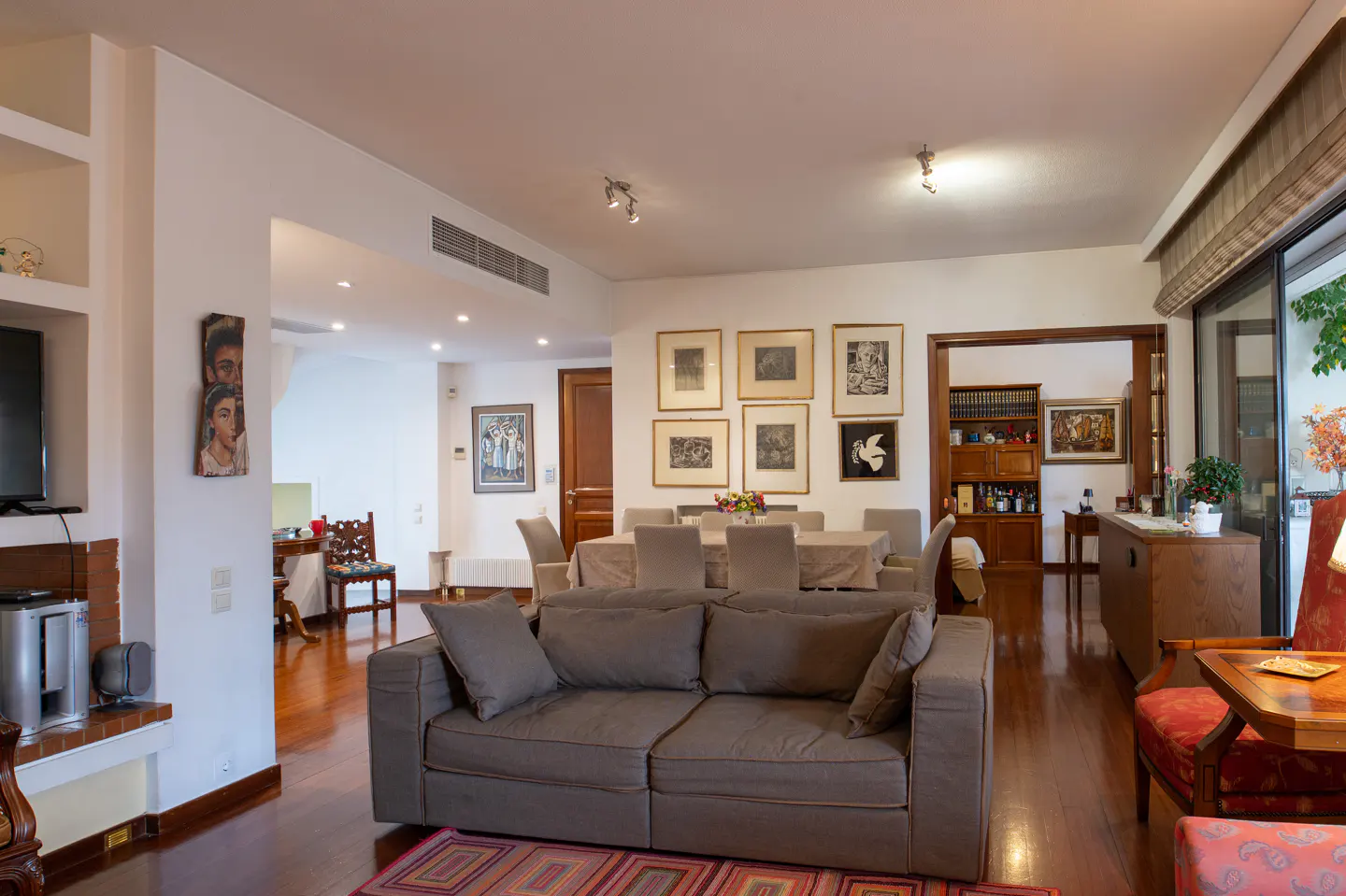 A bright, open-concept living and dining area with hardwood floors and neutral-toned furniture. Art adorns the walls.