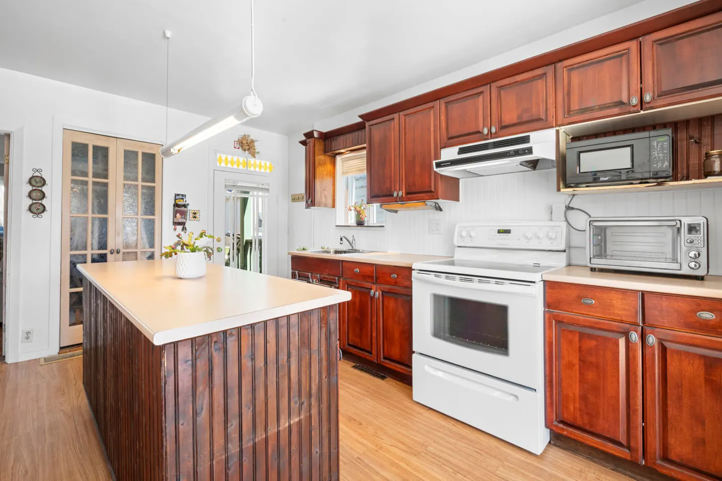 A kitchen with white walls, wood floors, and dark wood cabinets. A white stove and island are also visible.