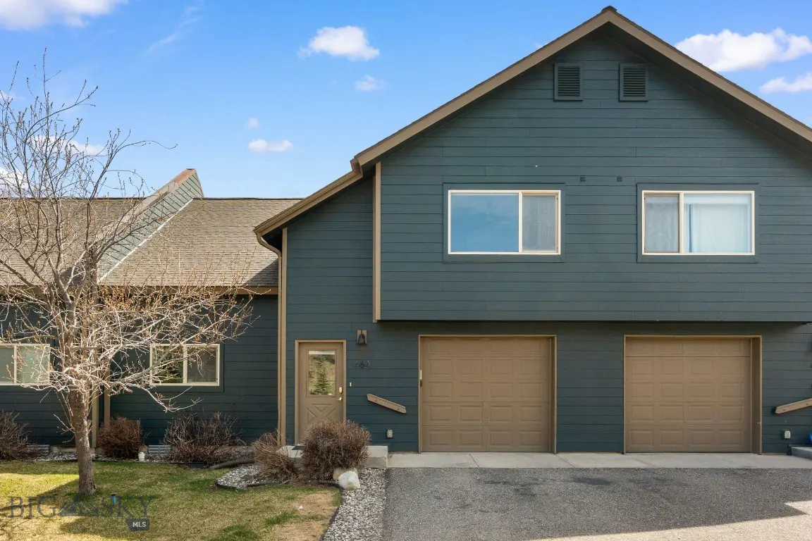 Exterior of a two-story townhouse with blue siding, brown trim, and two garage doors. A bare tree stands in the front yard.