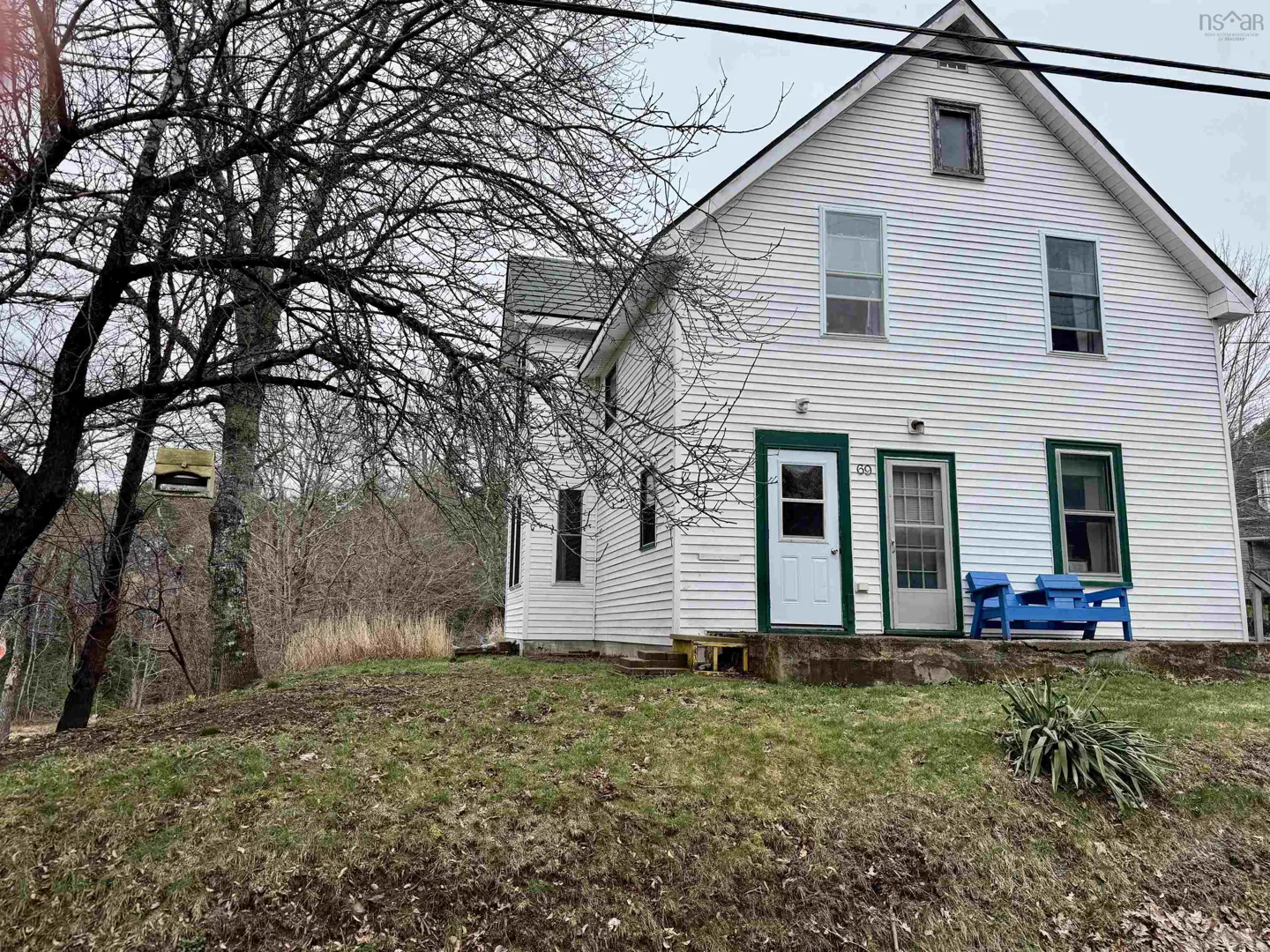 Two-story white house with green trim, two doors, and a blue bench on the porch. A large tree is on the left.
