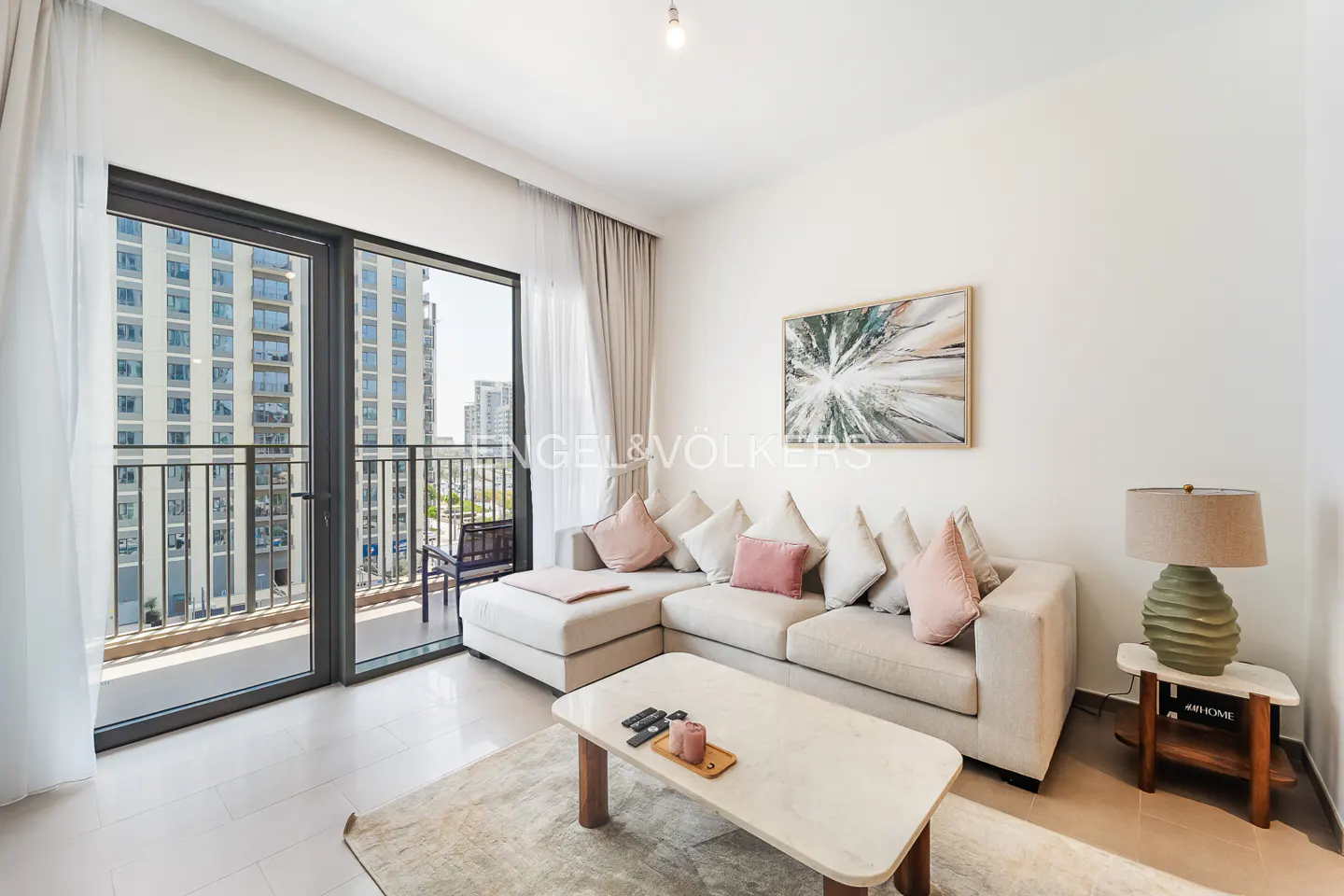 Modern living room with a beige sectional sofa, pink accent pillows, marble coffee table, and balcony view of city buildings.