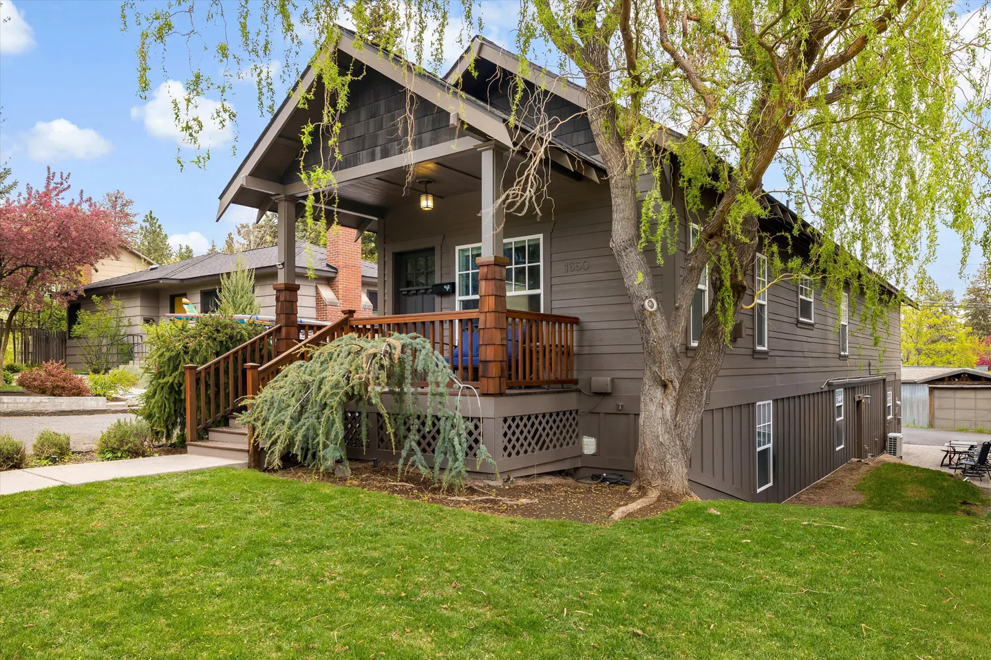 A two-story brown house with a porch and a green lawn on a sunny day.