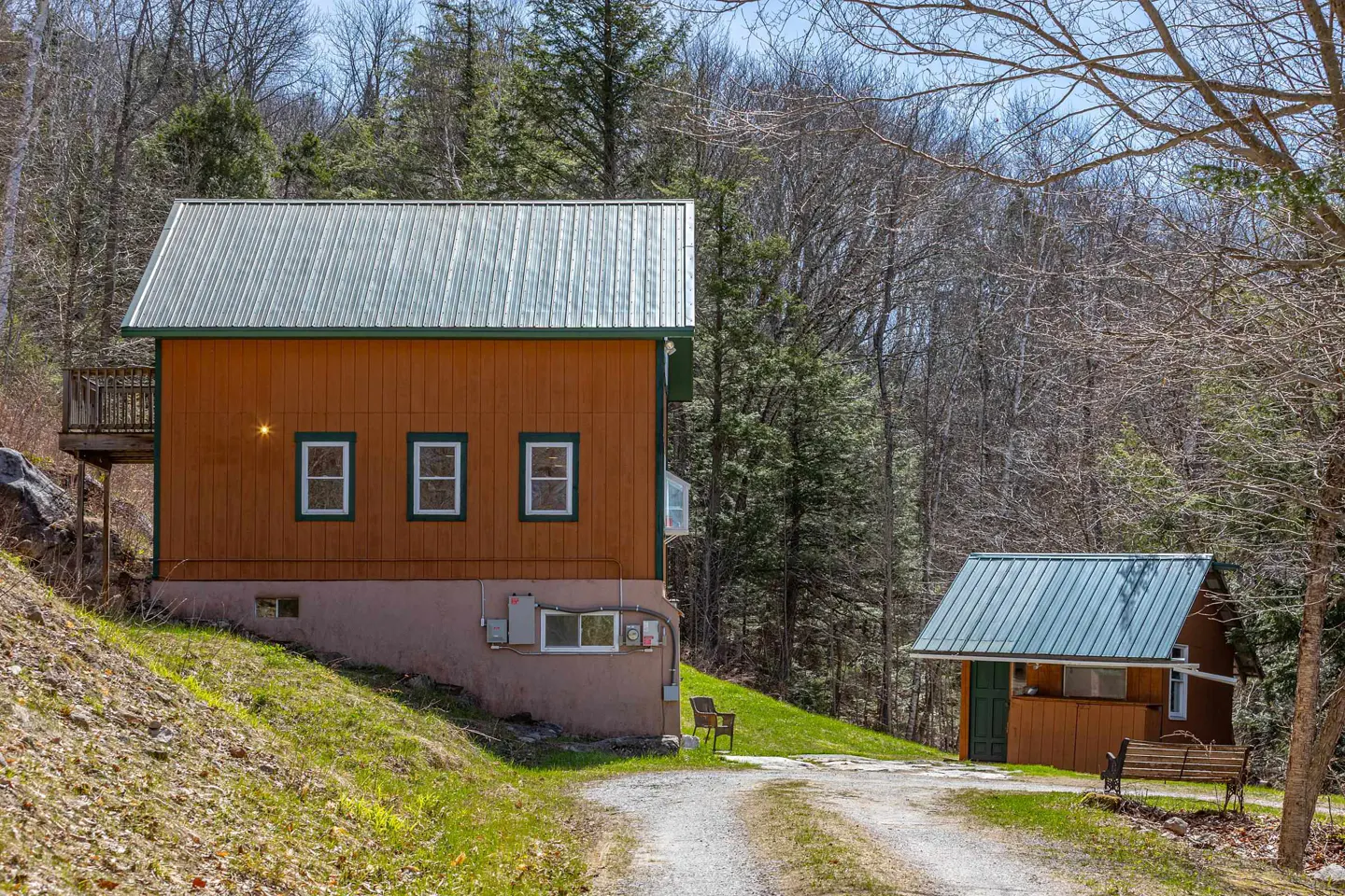 Exterior view of a two-story orange house with a metal roof, surrounded by trees and a smaller building.