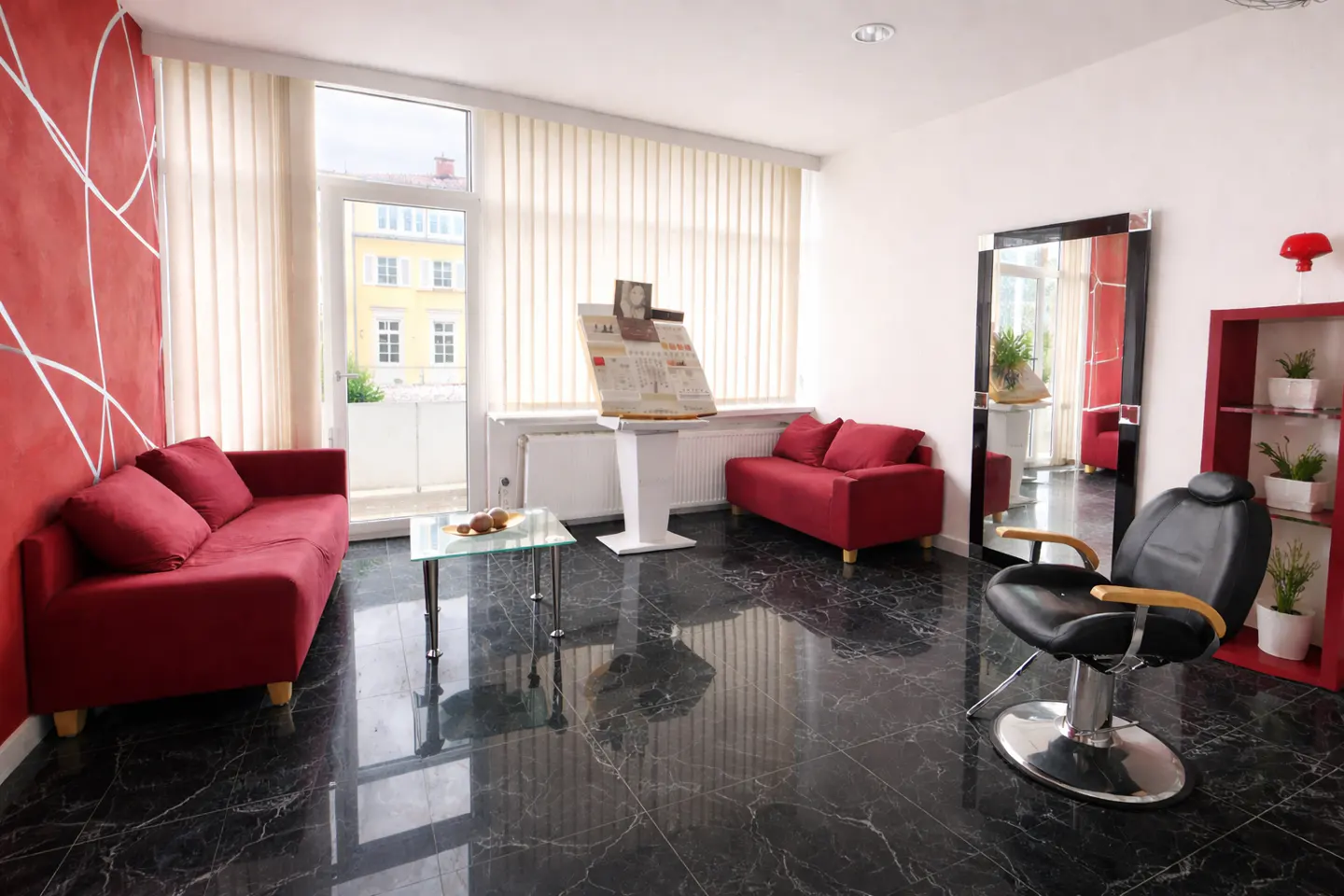 Salon waiting area with red sofas, black marble floors, and a barber chair. A large mirror reflects the room.