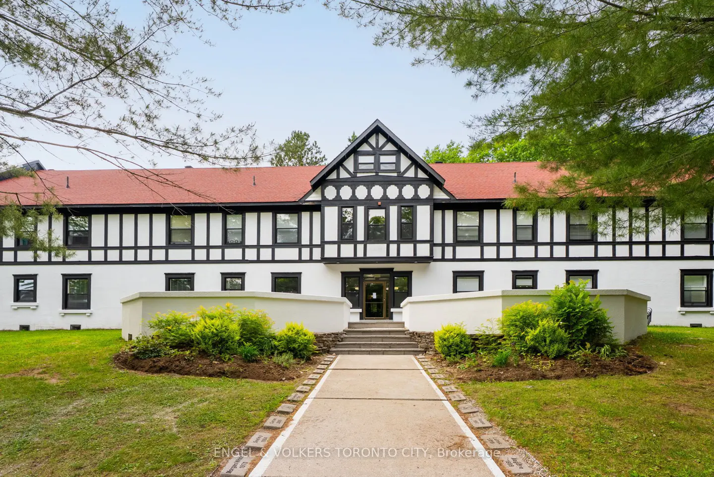 A two-story Tudor-style building with a red roof, white walls, and black trim, featuring a central walkway and landscaping.