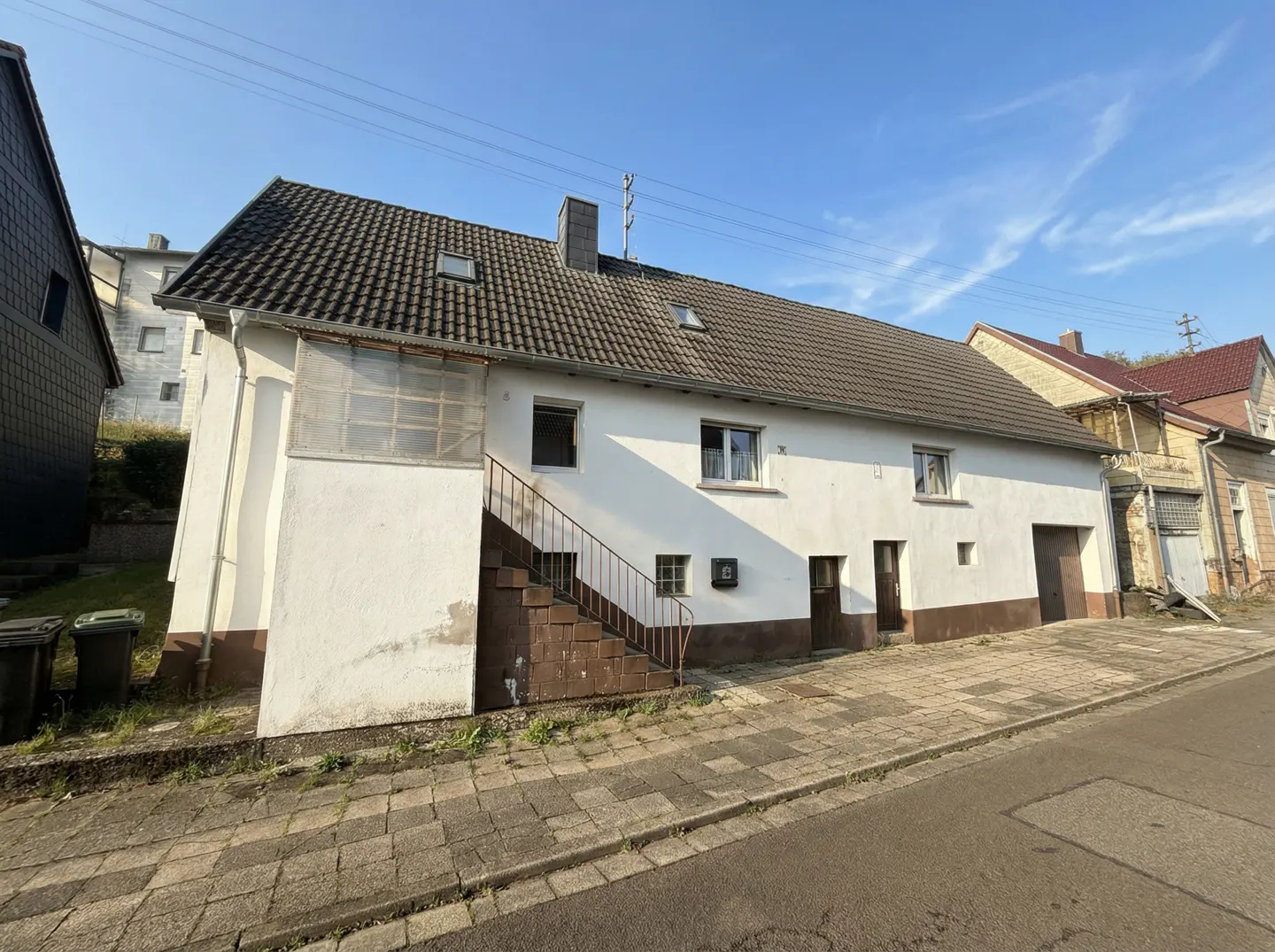 Exterior view of a two-story white house with a brown tiled roof and a brick staircase leading to the second floor.