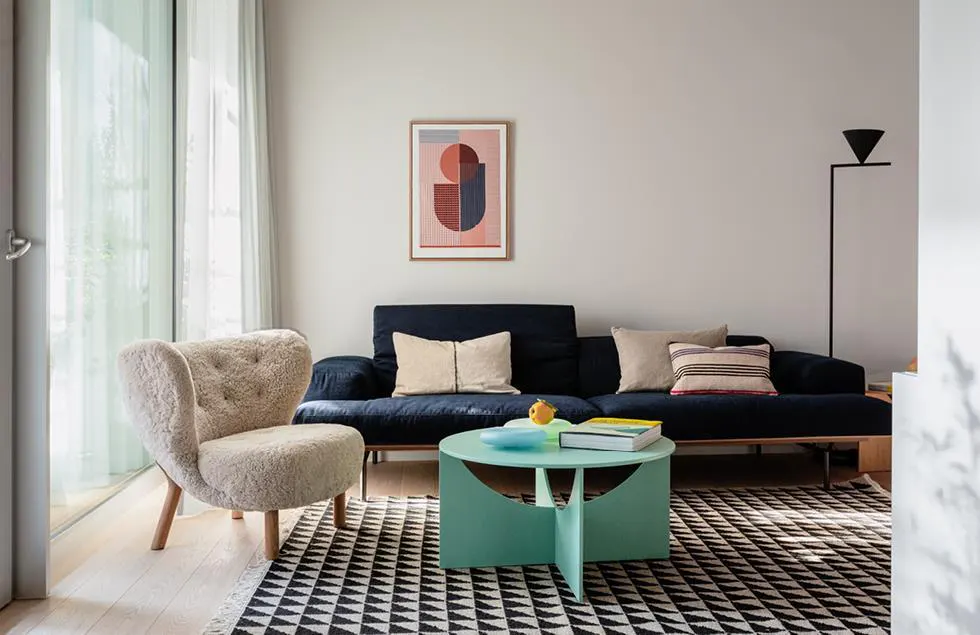 Living room with a navy sofa, a light-colored armchair, and a round mint-green coffee table on a black and white patterned rug.