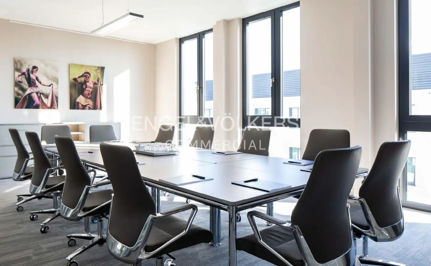 Bright conference room with a long table, black chairs, and large windows. Artwork hangs on the wall.