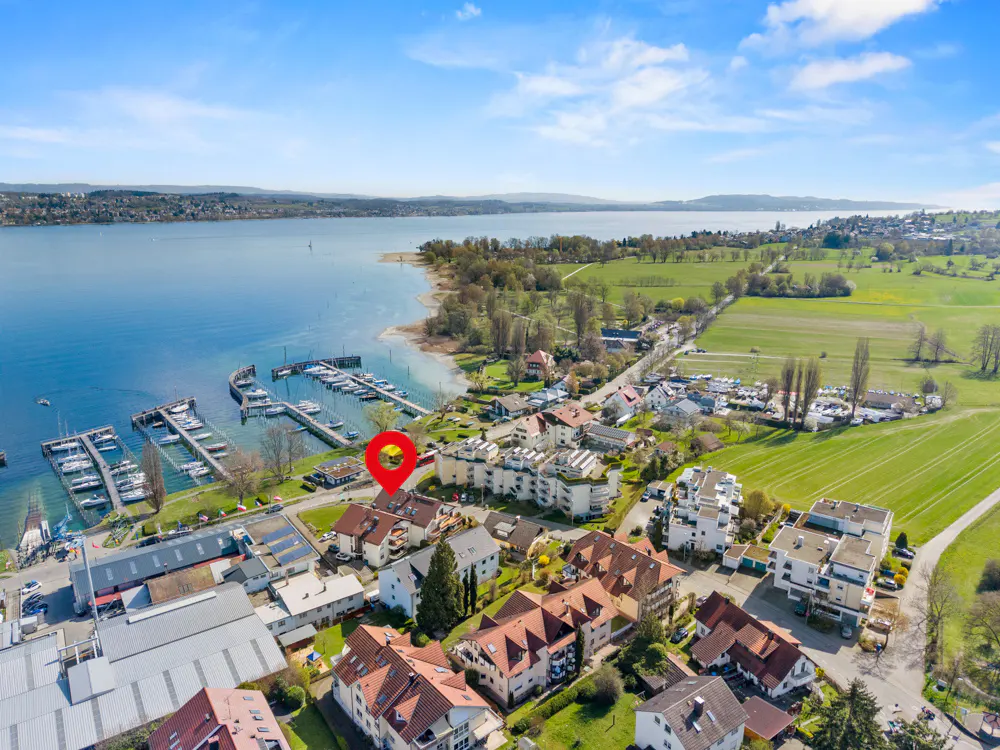 Aerial view of a lakeside town with a marina, houses with red roofs, and a red location pin on one of the houses.
