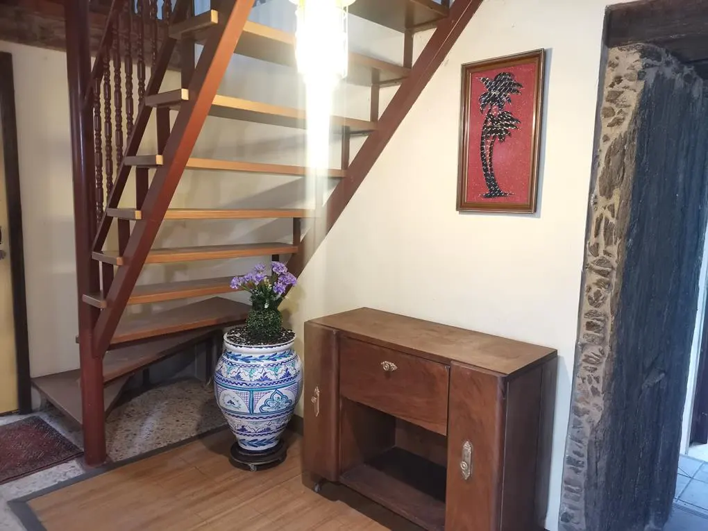Interior view of a home featuring a wooden staircase, cabinet, and a blue and white patterned vase with purple flowers. A framed palm tree art hangs on the wall.