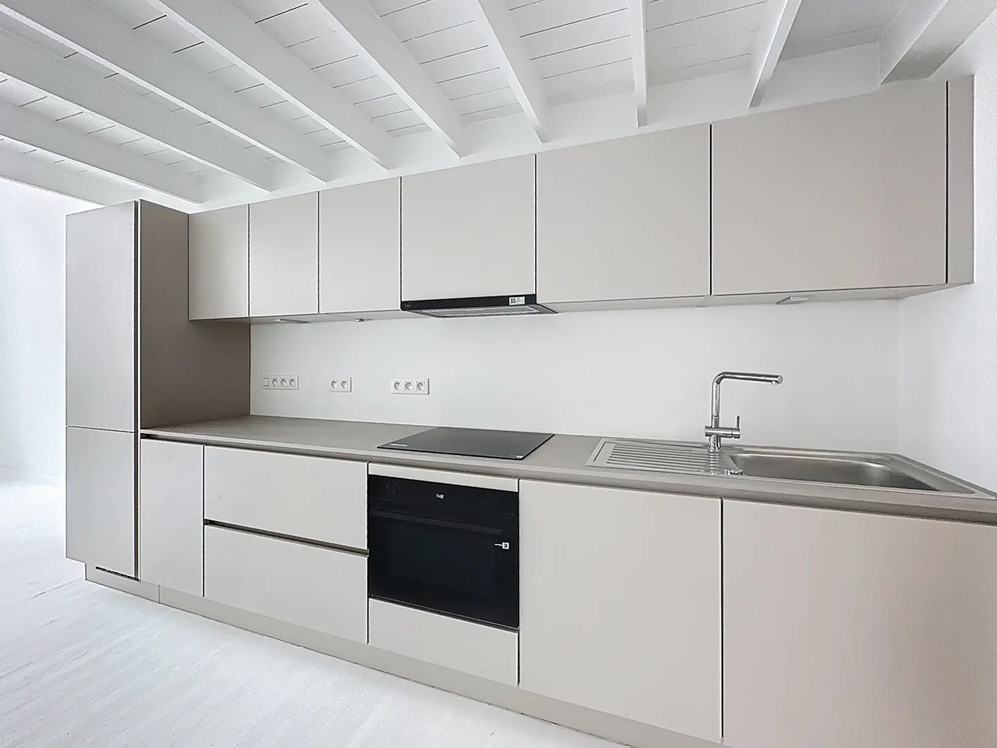 Bright kitchen with white ceiling beams, light gray cabinets, black oven, and stainless steel sink.