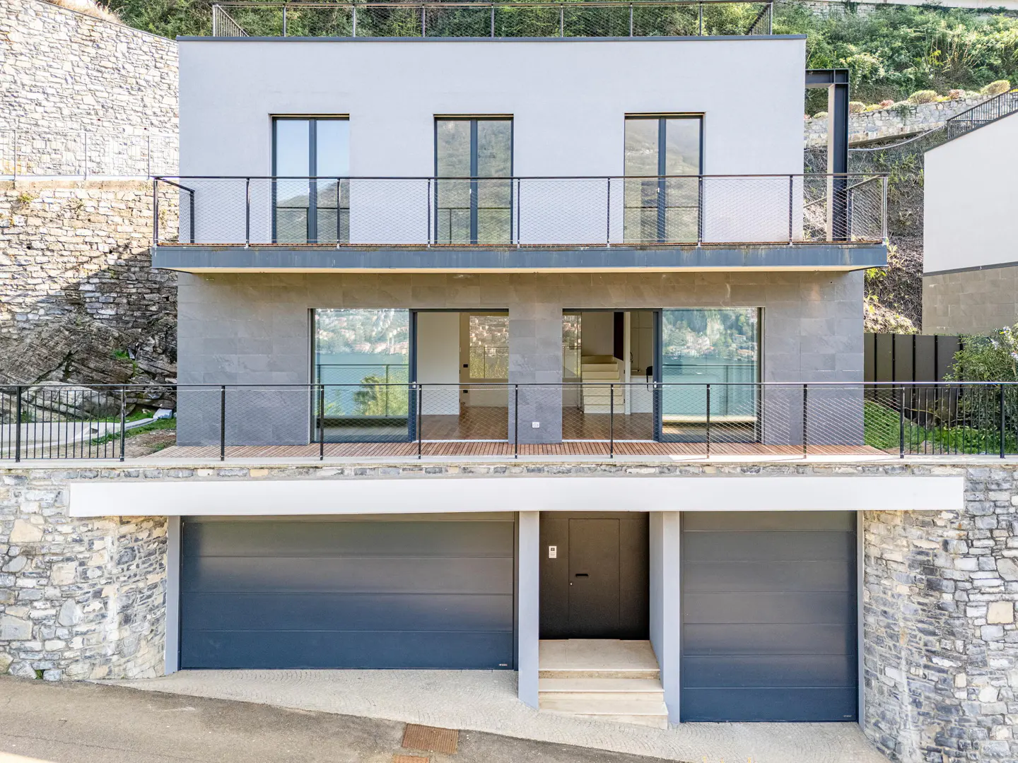 Modern three-story house with gray exterior, black framed windows, and a two-car garage built into a hillside.