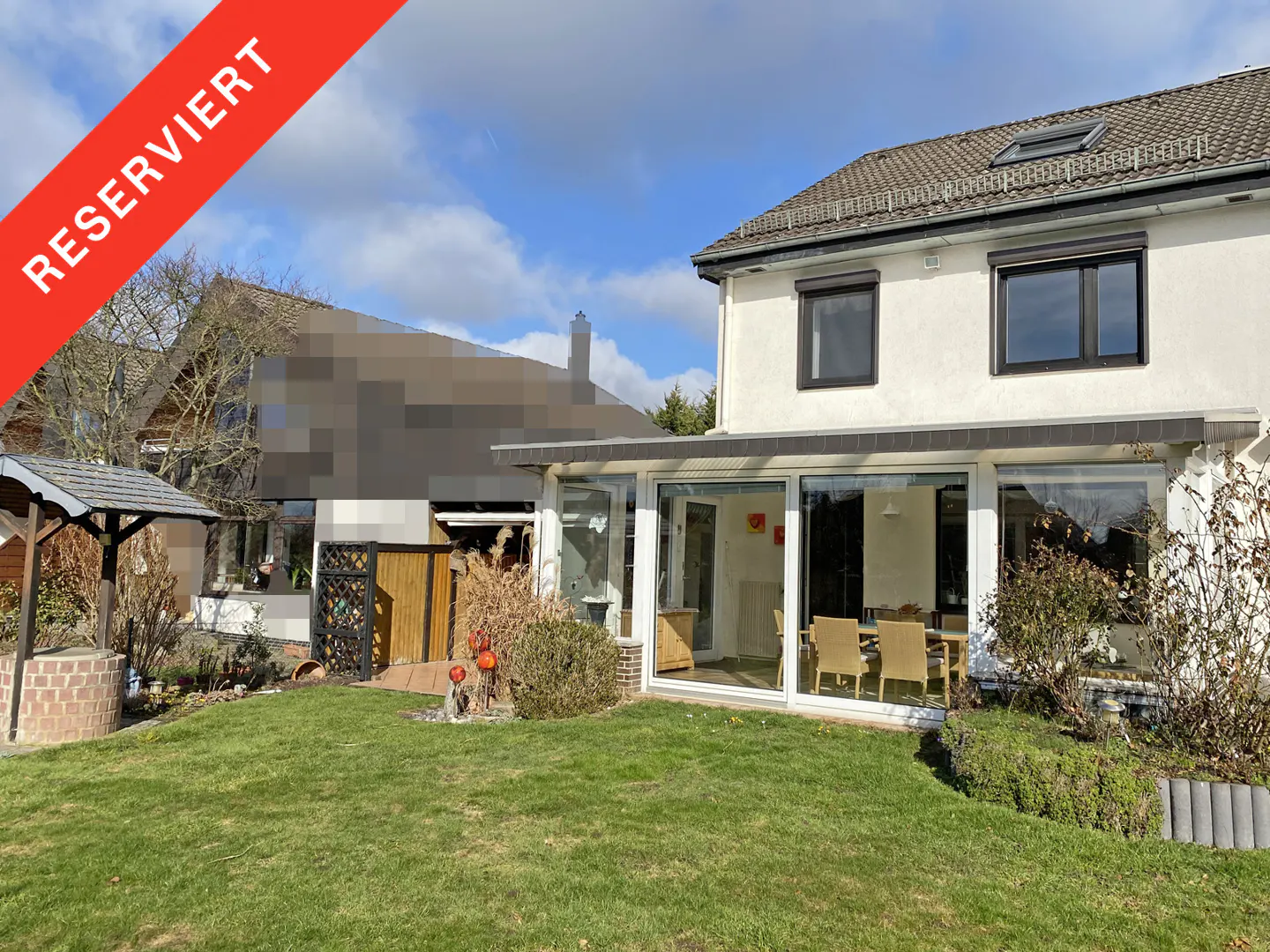 A two-story white house with a glass-enclosed patio and green lawn. A red banner with "Reserviert" is in the upper left corner.