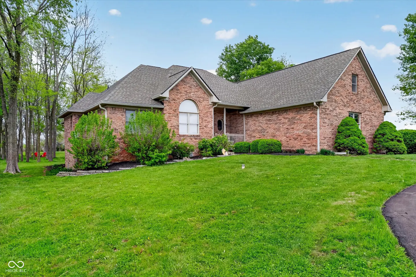 Brick house with a gray roof, green lawn, and trees under a blue sky.