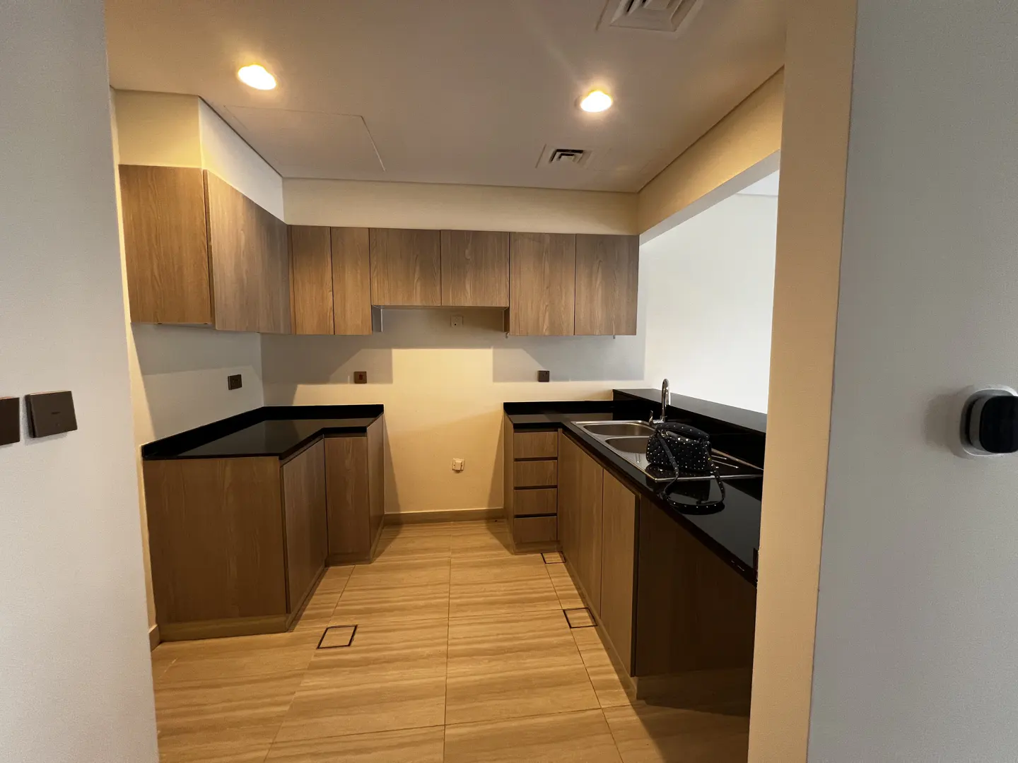 A bright kitchen with wood cabinets, black countertops, and tile floors. A sink and a purse are on the counter.