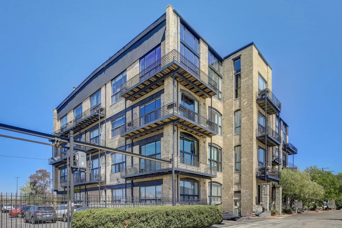 Exterior view of a multi-story brick apartment building with black balconies and large windows under a clear blue sky.