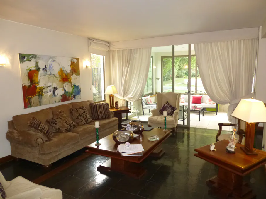 A living room with a brown sofa, a large colorful painting, and a glass door to a sunroom.