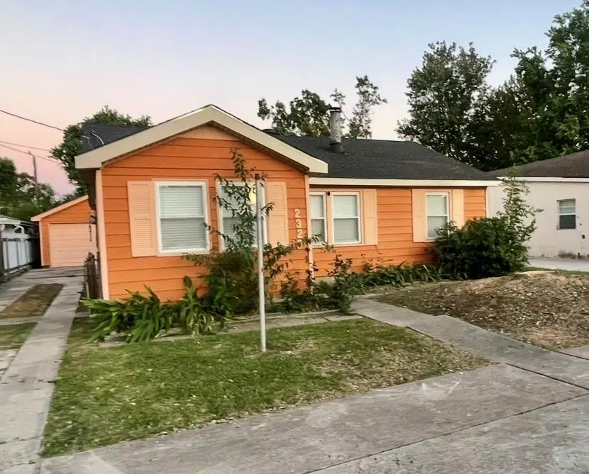 A single-story orange house with white trim and a black roof, viewed from the street. A detached garage is on the left.