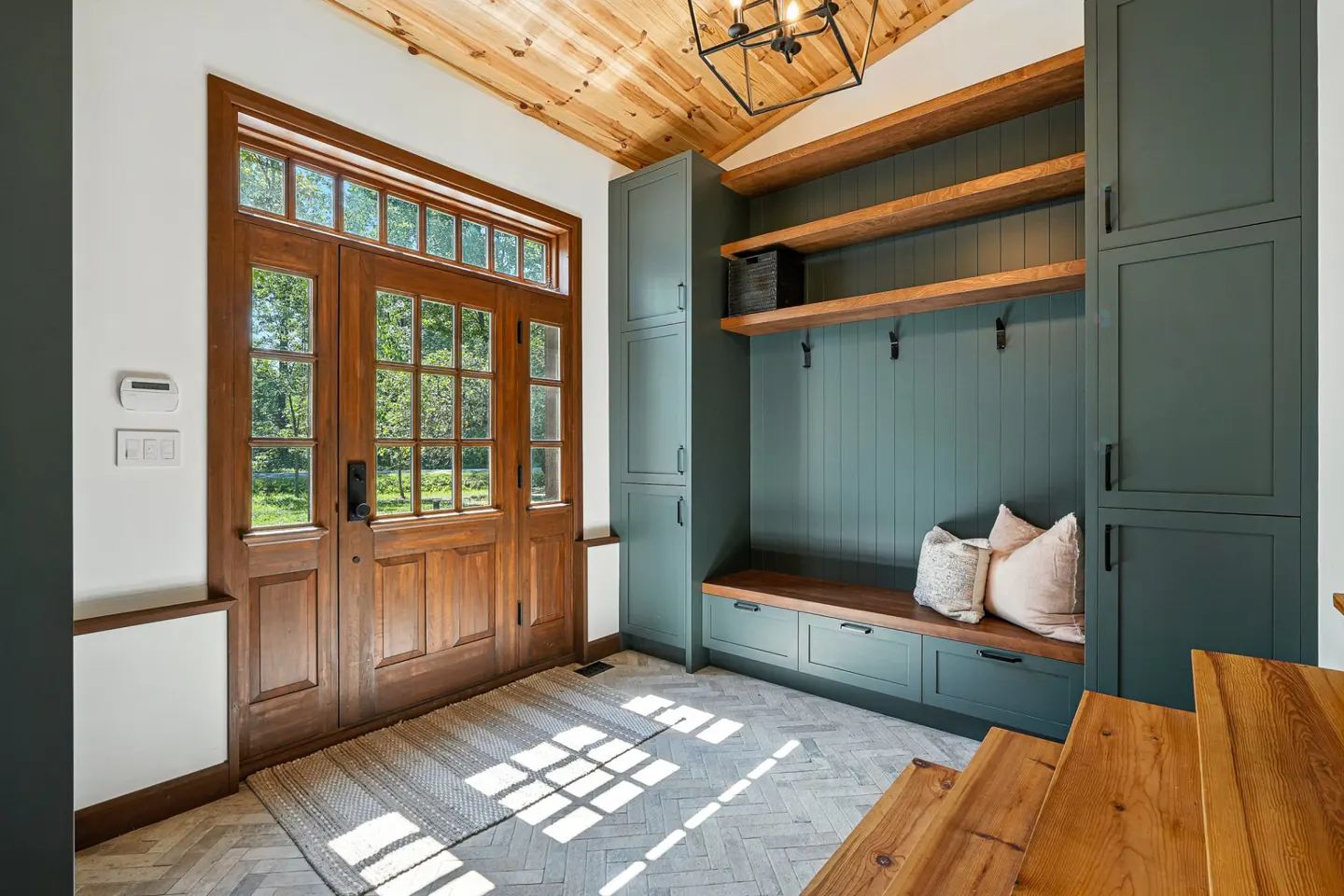 Entryway with wood door, herringbone floor, and green mudroom storage with wood shelves and bench.
