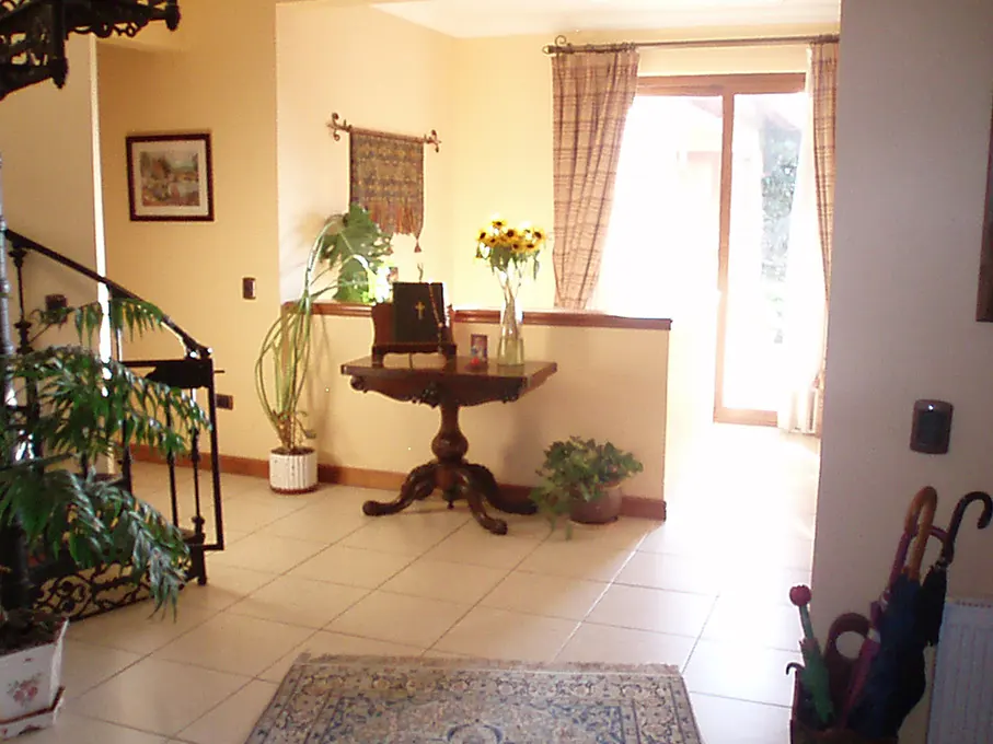 A foyer with beige tile floors, a dark wood table with sunflowers, and a staircase with potted plants.