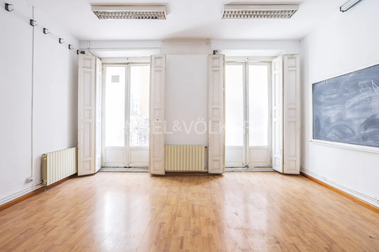 Bright, empty room with wood floors, white walls, and open white doors. A chalkboard is on the right wall.